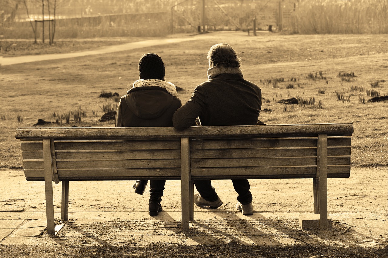 Un hombre y una mujer sentados en un banco, de espaldas, mirando hacia un parque invernal